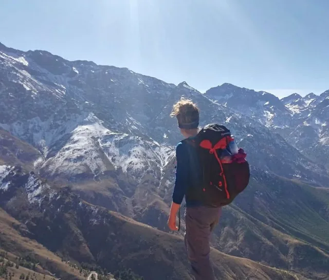 Wanderer mit rotem Rucksack blickt über einen verschneiten Gebirgskamm im Atlasgebirge