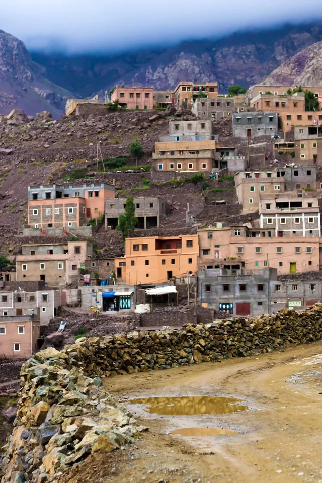 Pink and ochre Berber houses stacked up a steep Atlas hillside beneath low cloud