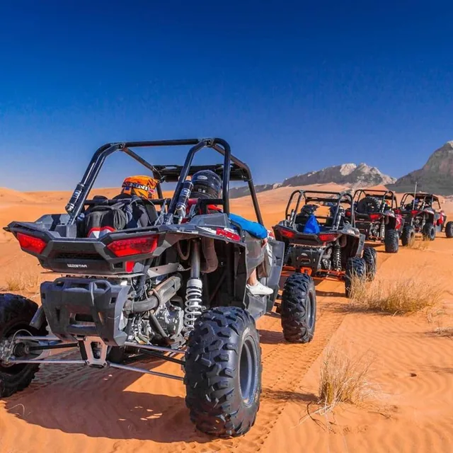 A convoy of buggies lined up on a desert track with rocky hills in the distance