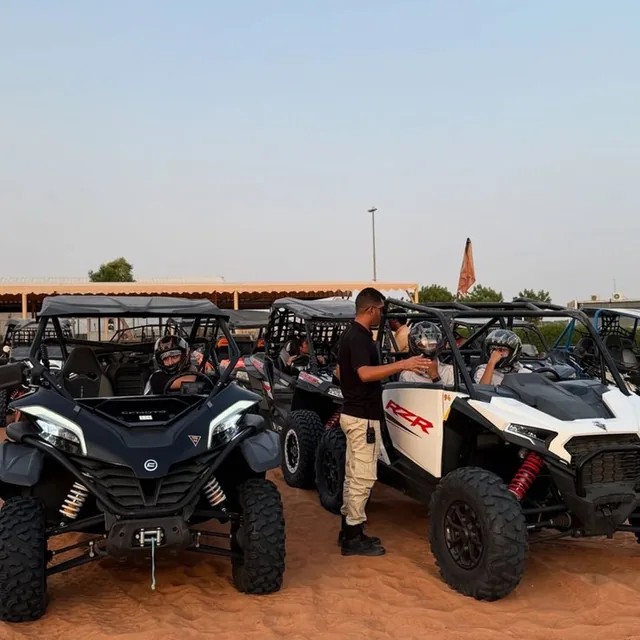 A guide giving a safety briefing to helmeted guests beside a fleet of buggies at the base