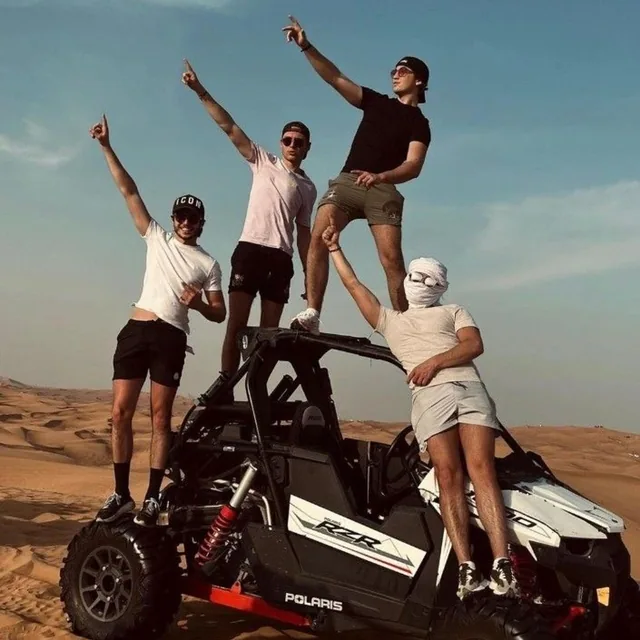 A group of friends celebrating on and around their buggy in the desert