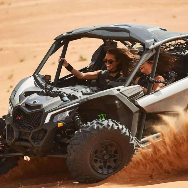 Two riders laughing in a two-seater buggy as it throws up a plume of dust on a desert turn
