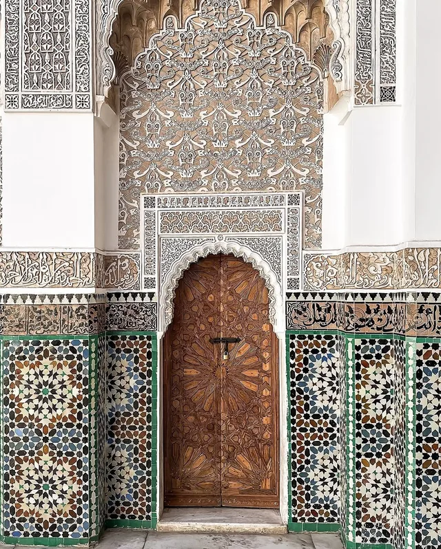 A carved cedar door framed by stucco calligraphy and zellige tilework at Medersa Ben Youssef