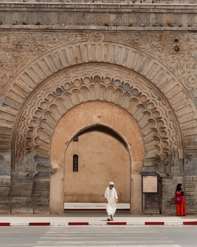 A man in a white djellaba walking through the carved stone gateway of the Marrakech city wall