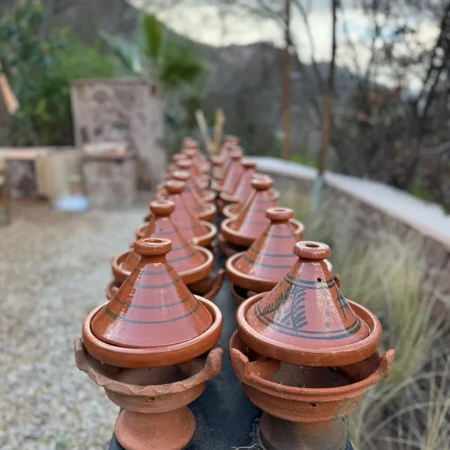 A row of painted clay tagines resting on charcoal braziers outdoors, ready for a cooking class