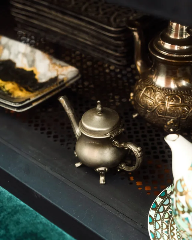 Teteras de plata marroquíes y platos de servir dispuestos en un estante oscuro en la cocina del riad