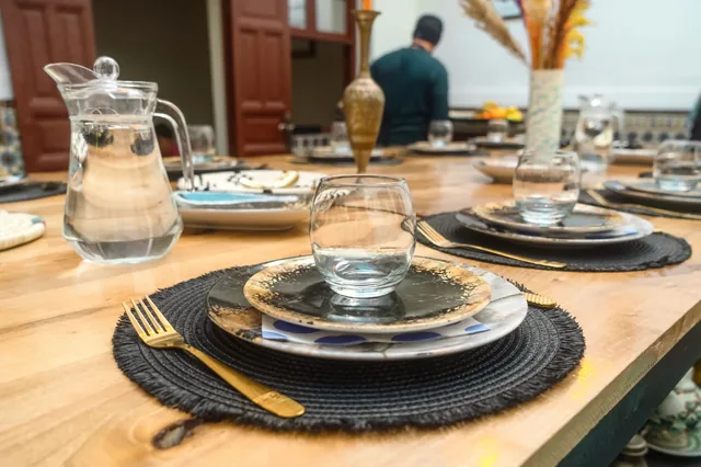 Detalle de la mesa de madera del riad con platos jaspeados, un vaso de agua y cubiertos dorados