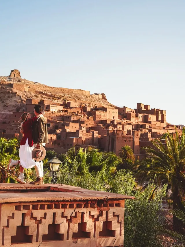A couple on a terrace at golden hour with the whole ksar of Aït Ben Haddou glowing behind