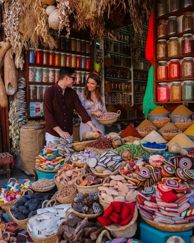 A couple browsing baskets of spices, herbs and rose petals at a Marrakech apothecary stall