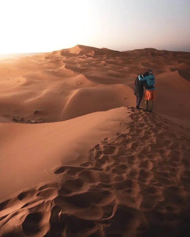 A couple standing arm in arm on a dune crest watching sunrise over the Sahara
