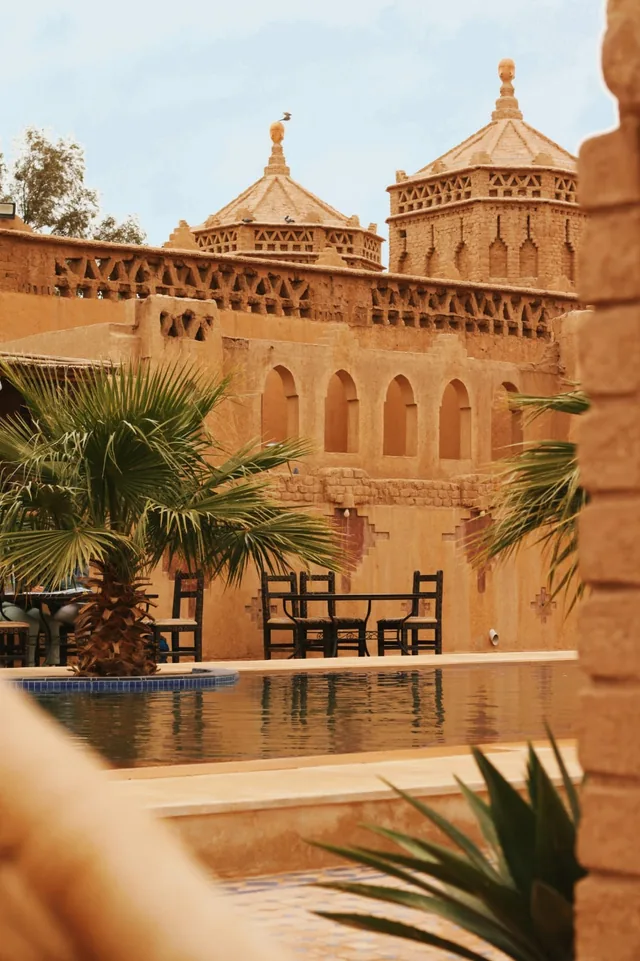 Pool und Palmen vor einem kunstvoll verzierten Kasbah-Hotel aus Lehm