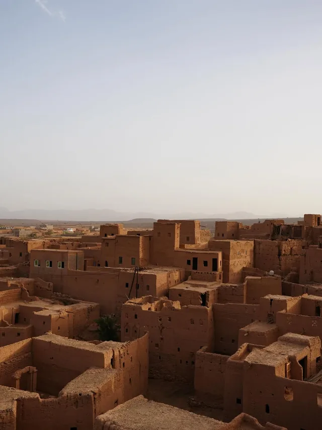 Earthen kasbah rooftops of a southern Moroccan village glowing at dusk with hills beyond