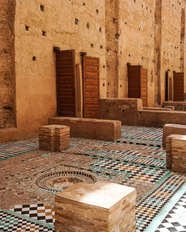 Carved cedar doors and patterned zellige paving in a sunlit court of El Badi Palace