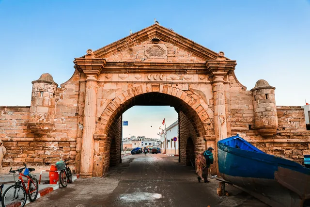 Das kunstvoll verzierte Hafentor Bab el Marsa in Essaouira mit einem blauen Boot daneben