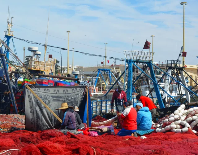 Fischer flicken leuchtend rote Netze zwischen Trawlern im Hafen von Essaouira