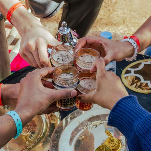 Four hands clinking decorated glasses of mint tea over a silver tray outdoors