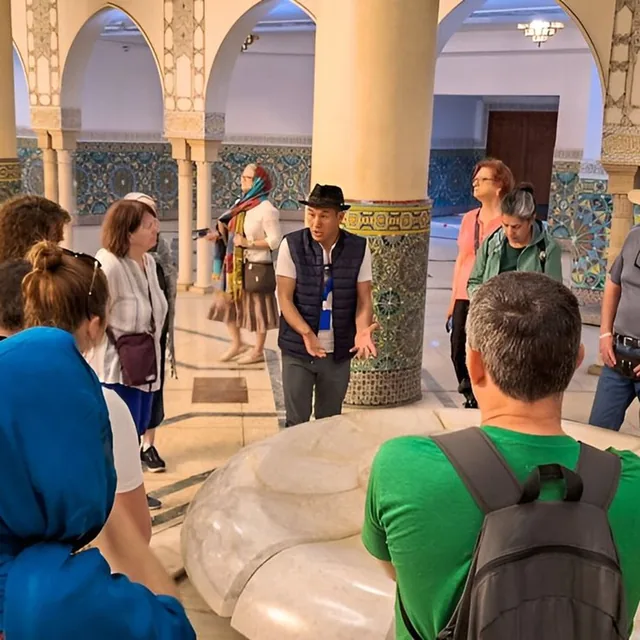 A guide explaining zellige tilework and marble to a small group inside a Moroccan monument