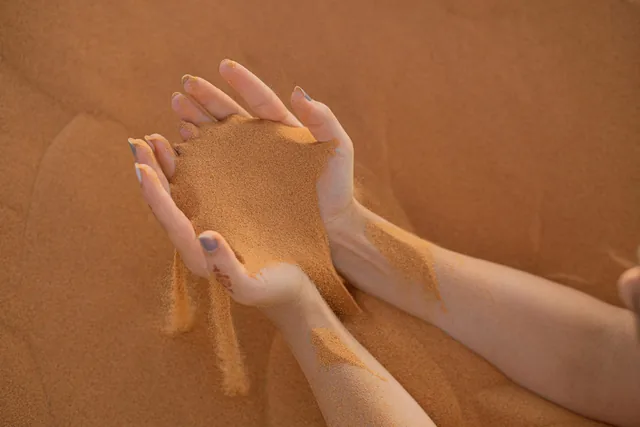 Hands letting fine orange Sahara sand fall through the fingers on a dune