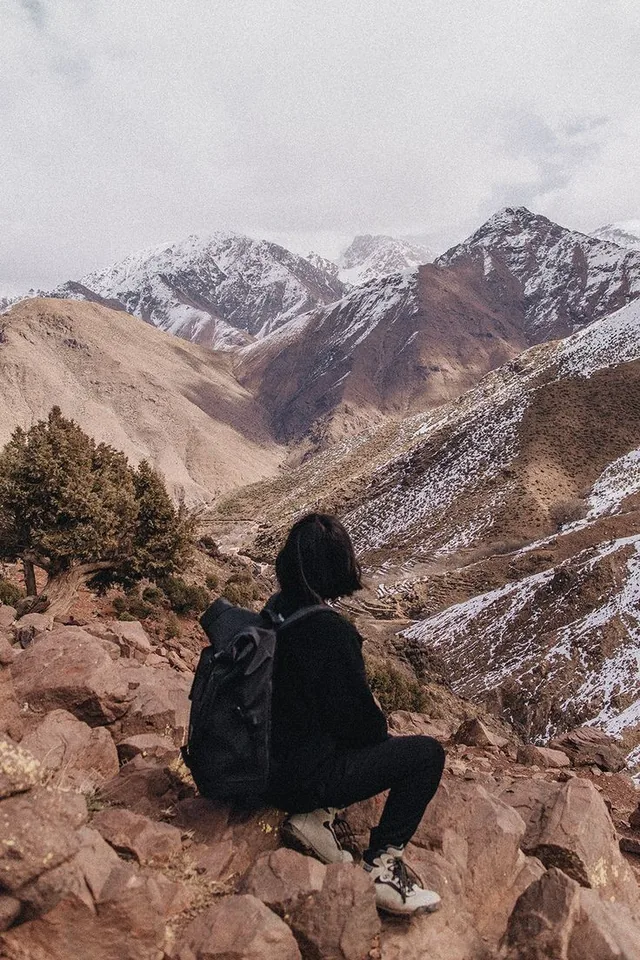 A walker sitting on rocks looking across a High Atlas valley with snow on the peaks