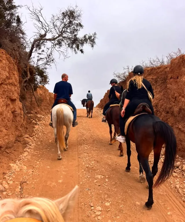 A small group riding horses along a red-earth track cut between banks near Marrakech