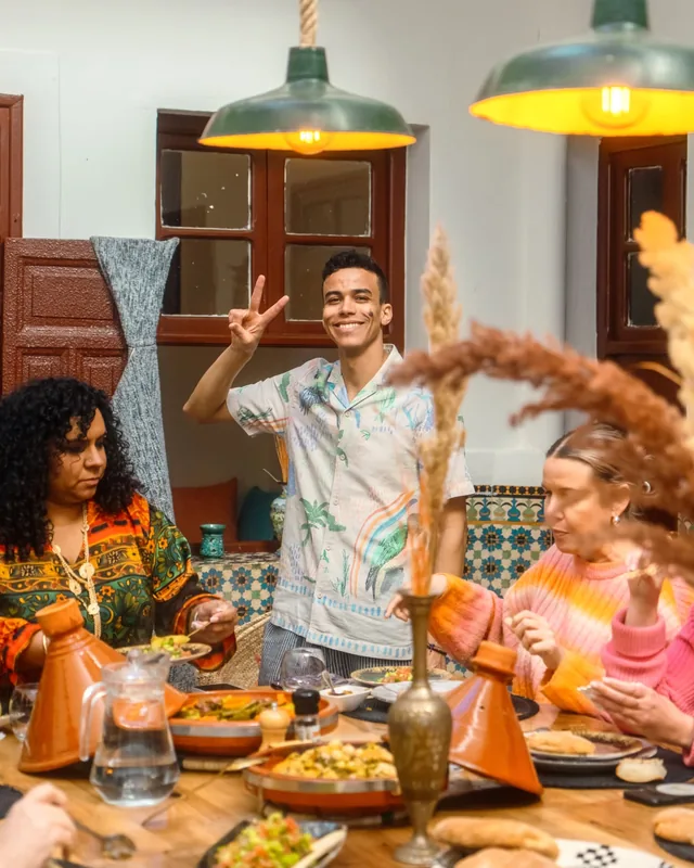 A smiling host welcoming guests around a riad dinner table set with tagines and bread