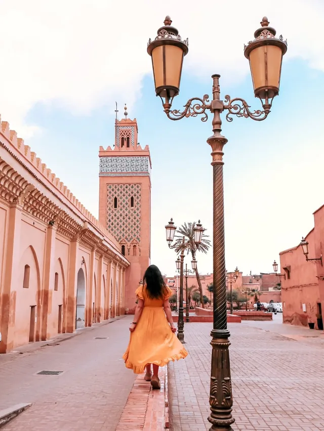 The tiled minaret of the Kasbah mosque above a pink Marrakech street with ornate lamp posts