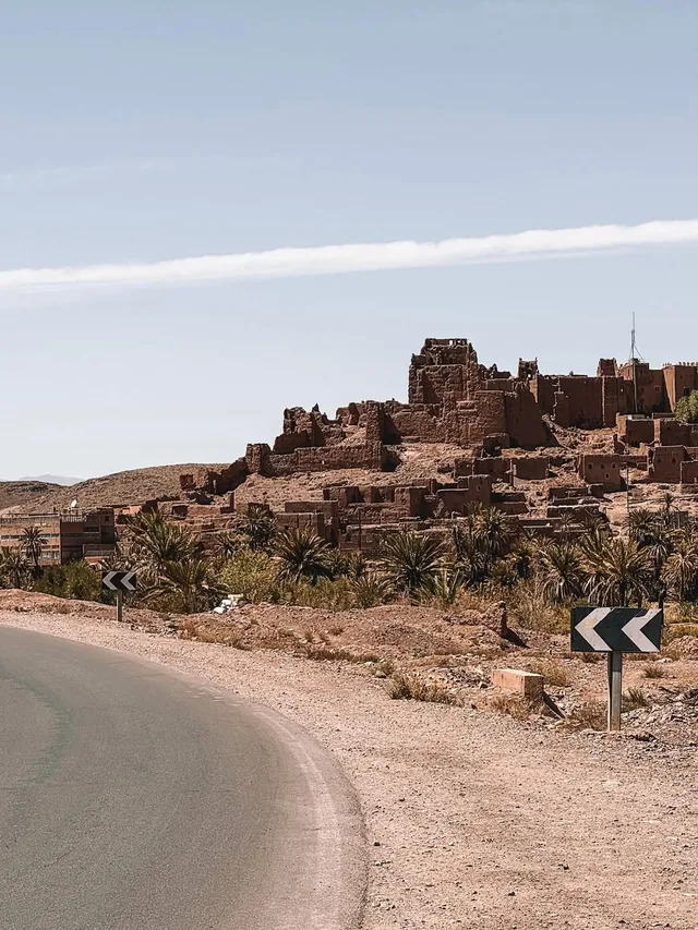Ruined kasbah walls rising above palm gardens beside the road towards Ouarzazate
