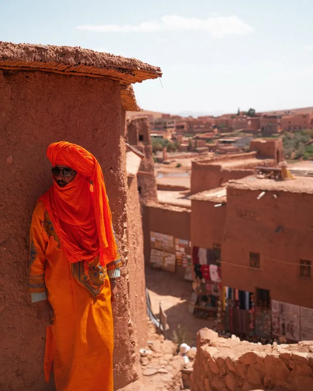 A local man in an orange djellaba and turban standing in a lane of the Aït Ben Haddou ksar