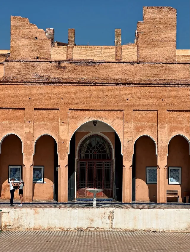Row of pointed arches and a tiled fountain in a red earthen Marrakech courtyard building