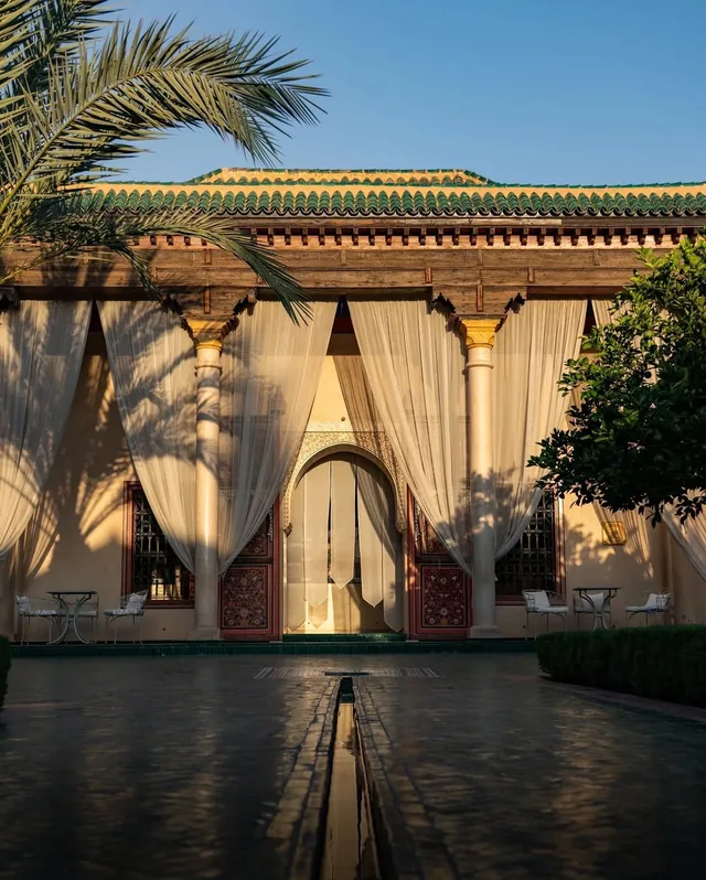 A tiled garden pavilion with white drapes and a carved doorway reflected in a still water channel