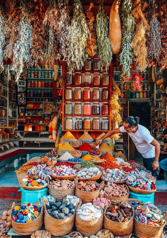 A Marrakech herbalist arranging spice cones, jars and baskets of minerals and soaps