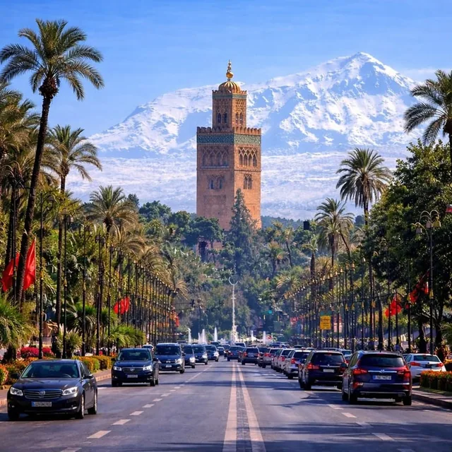 The Koutoubia minaret framed by palm-lined avenue traffic with the snow-covered Atlas mountains behind
