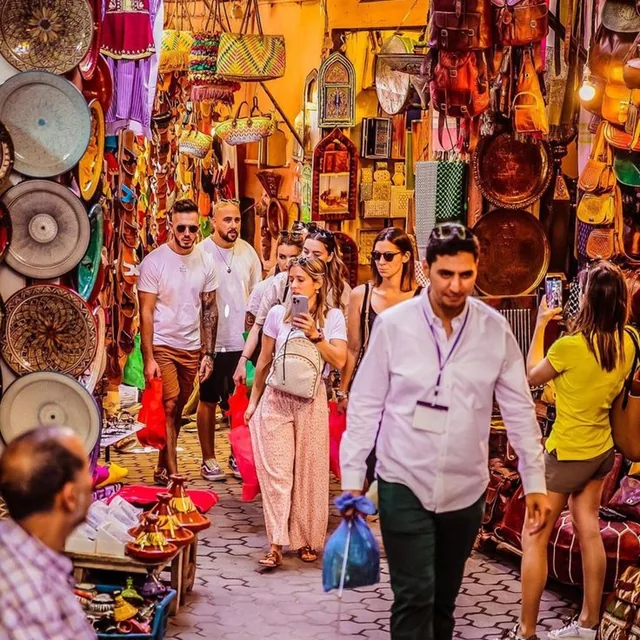 A local guide leading visitors through a Marrakech souk alley lined with lanterns, leather bags and painted plates