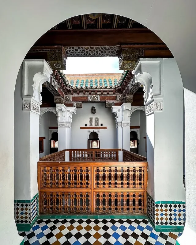 Carved wooden galleries and mosaic floors seen through an arch at Medersa Ben Youssef