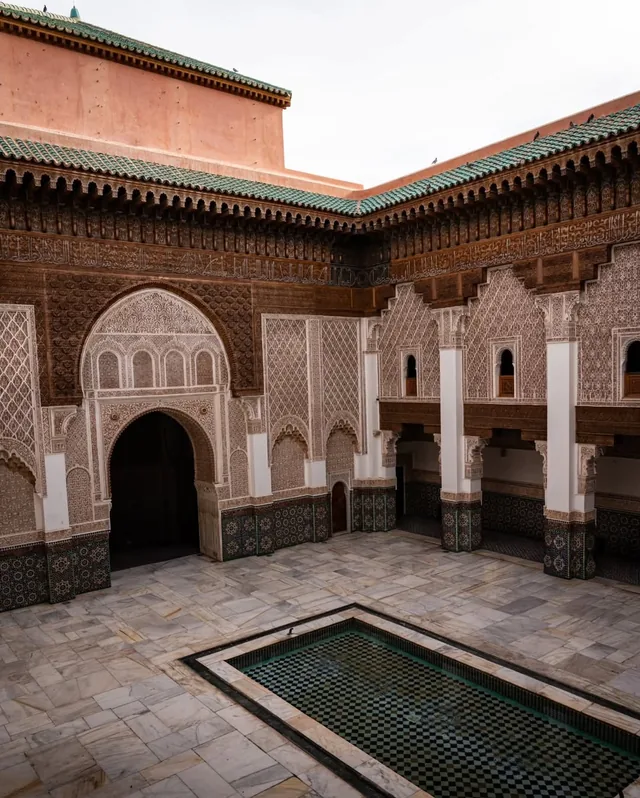 The wide marble courtyard of the Medersa Ben Youssef with carved cedar galleries and a green-tiled roof
