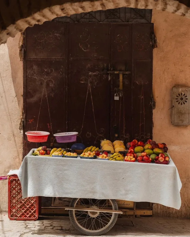 A fruit cart piled with peaches, bananas and mangoes standing outside an old studded door in the medina