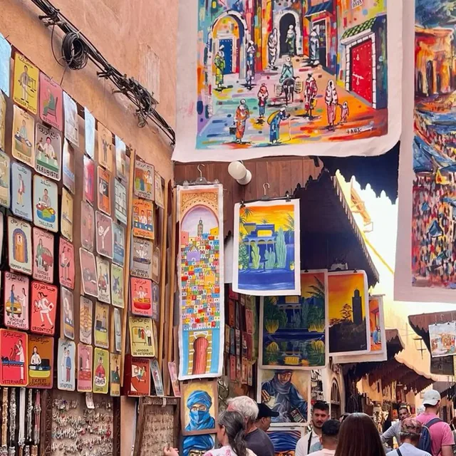 Visitors browsing hand-painted signs and canvases in a narrow Marrakech art lane