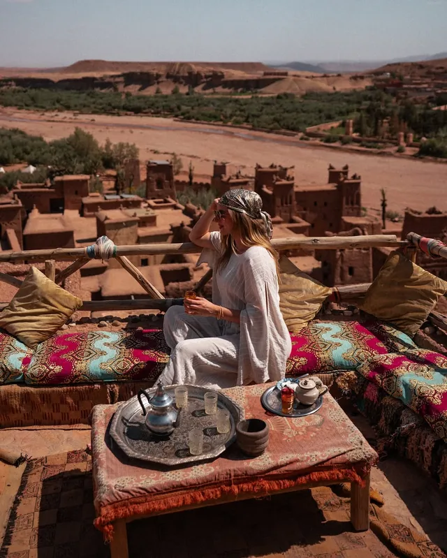 A guest with a glass of mint tea on a cushioned kasbah terrace above Aït Ben Haddou