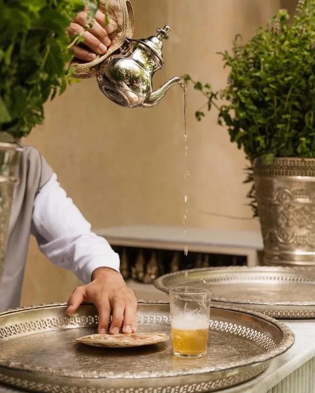Mint tea poured from a silver teapot into a glass on an engraved silver tray