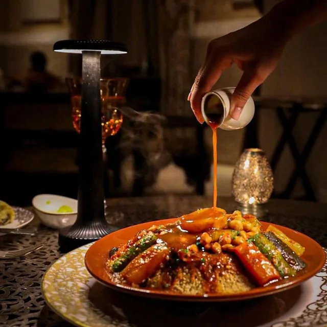 Sauce being poured over a couscous dish with vegetables at a candlelit evening table