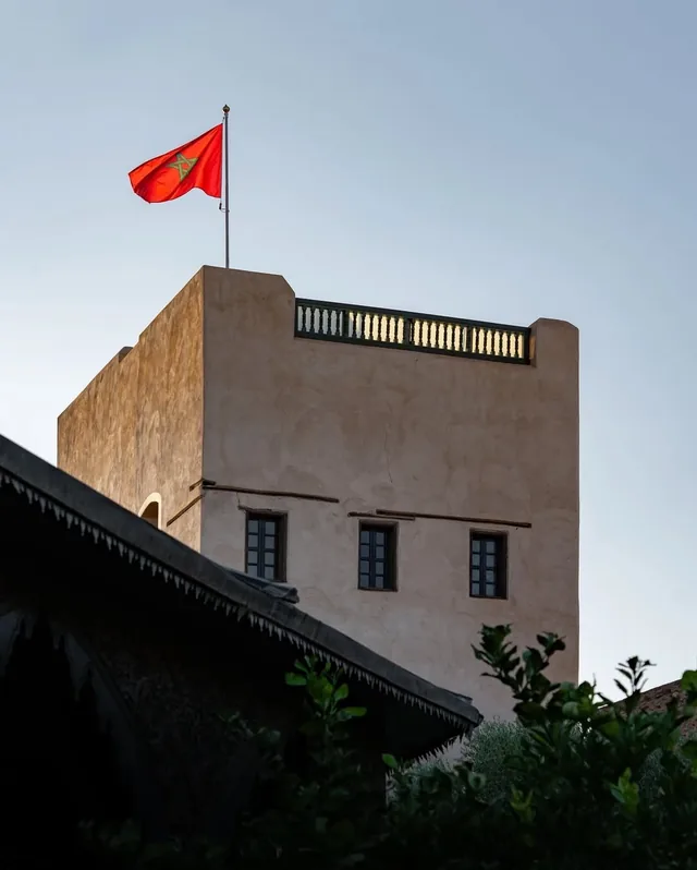 A Moroccan flag flying above an earthen garden tower at golden hour