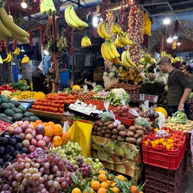 A covered Moroccan market hall stacked with grapes, oranges, tomatoes, peppers and hanging bananas