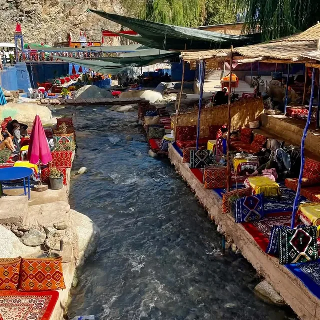 Reed-shaded café terraces with Berber rugs lining both banks of the Ourika river