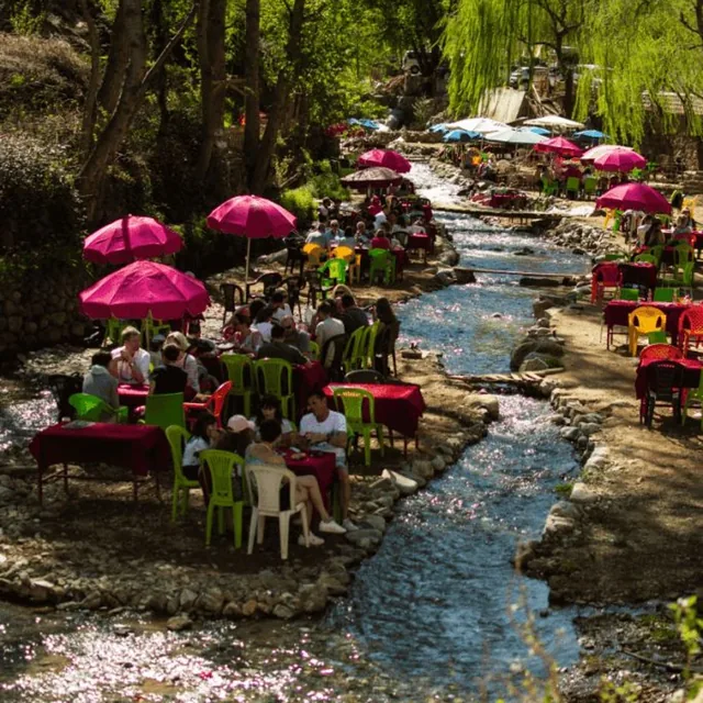 Guests eating at pink-parasol tables set on both banks of the Ourika river in spring