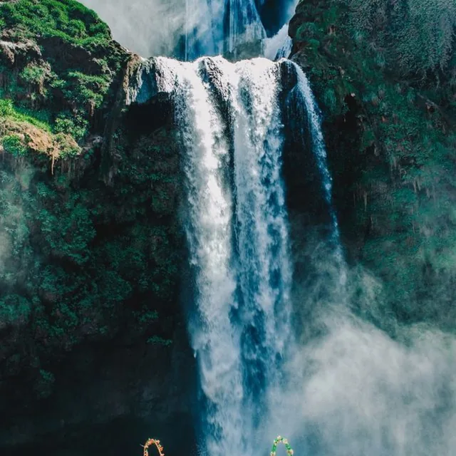 Close view of the Ouzoud waterfall falling through mist and green cliffside vegetation