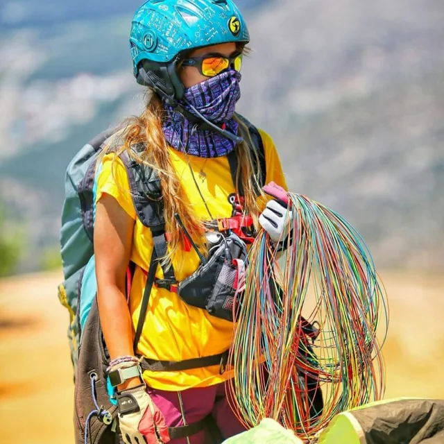 A paraglider pilot in helmet, goggles and harness gathering the coloured lines of a wing before launch