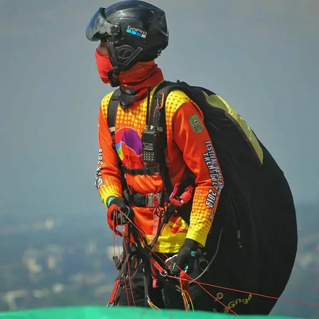 A paragliding pilot in a harness with a radio on the chest strap holding the risers before take-off