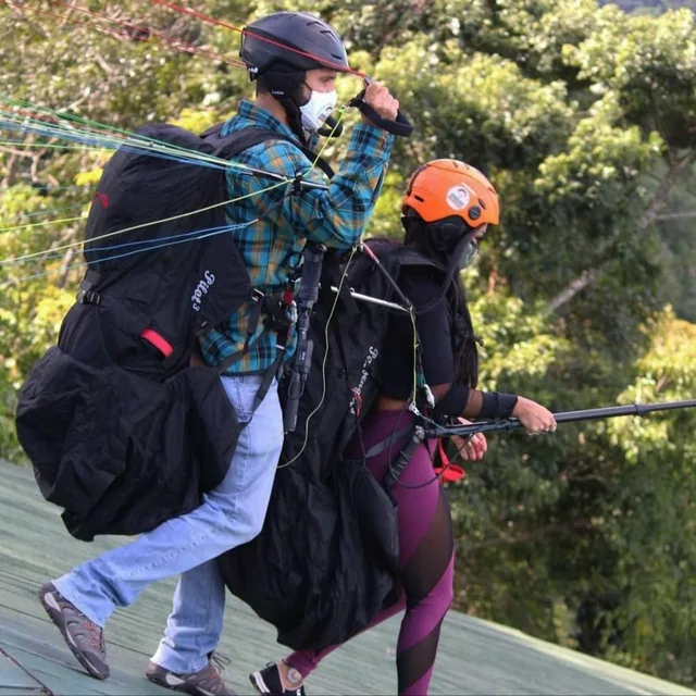 A tandem paragliding pilot and passenger in helmets walking to the launch ramp with the wing and lines laid out