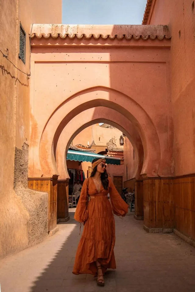 A visitor walking through a pink-plastered horseshoe archway in the Marrakech medina