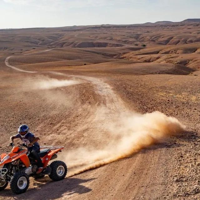 A quad bike throwing up a long trail of dust on a desert track through rolling hills